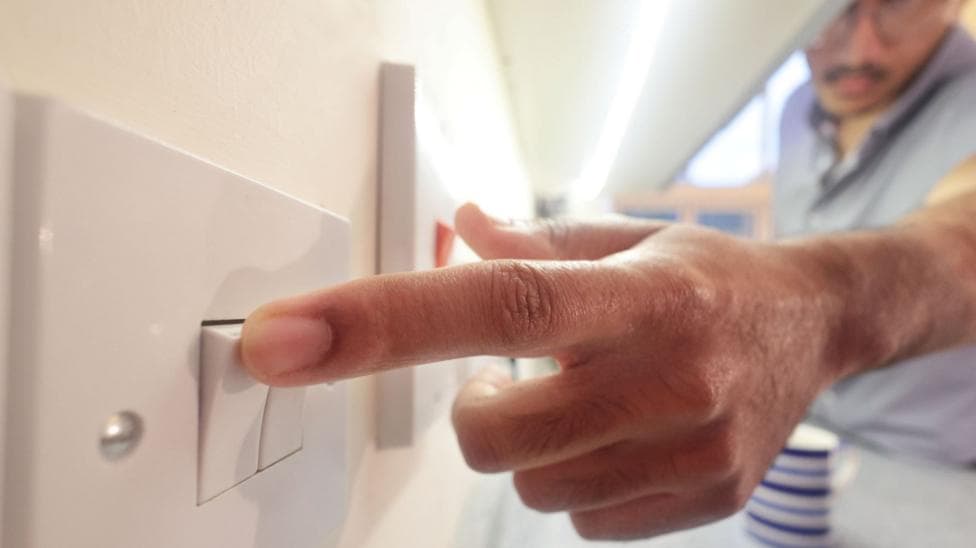 A man's hand switching on a white light switch.