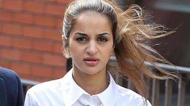 A woman in a white collared shirt walks outside court, her ponytail blown sideways by the wind, with a brick building and metal railing behind them.