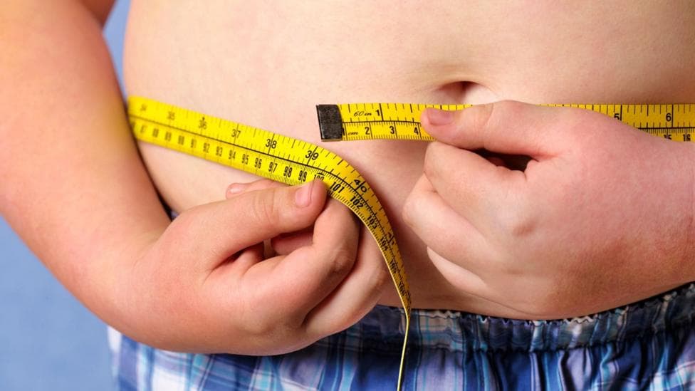 A child with a large waste has a tape measure tied around it. The photo is posed by a model
