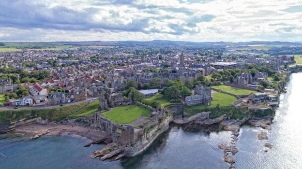 A birds eye view of St Andrews with a ruined cathedral next to the sea in the foreground, and the rest of the town in the background