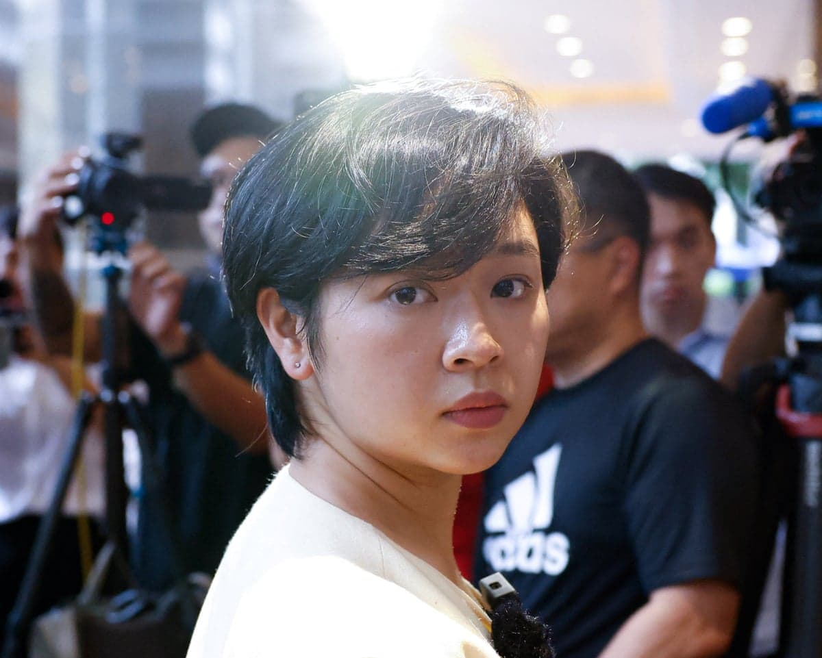 Selina Cheng looks over her shoulder amid reporters holding cameras and microphones