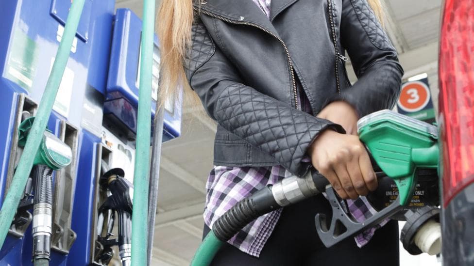 Person wearing a black leather jacket filling up their car from the petrol pump