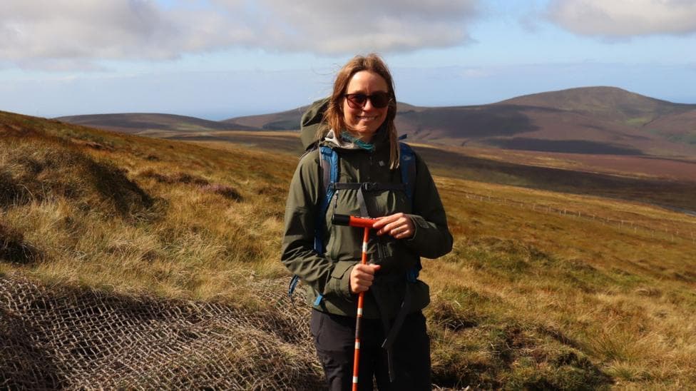 Sarah smiles in the background are the rolling hills of the Isle of Man