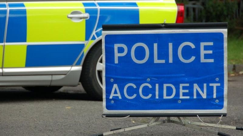 Blue police sign with Police Accident written in white writing. It is next to a police car