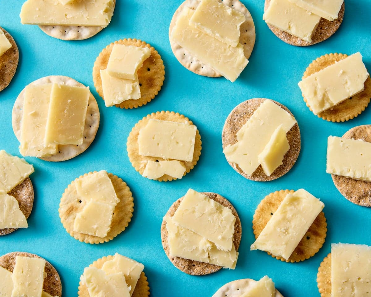 Overhead view of round crackers topped with slices of cheddar cheese on a blue background