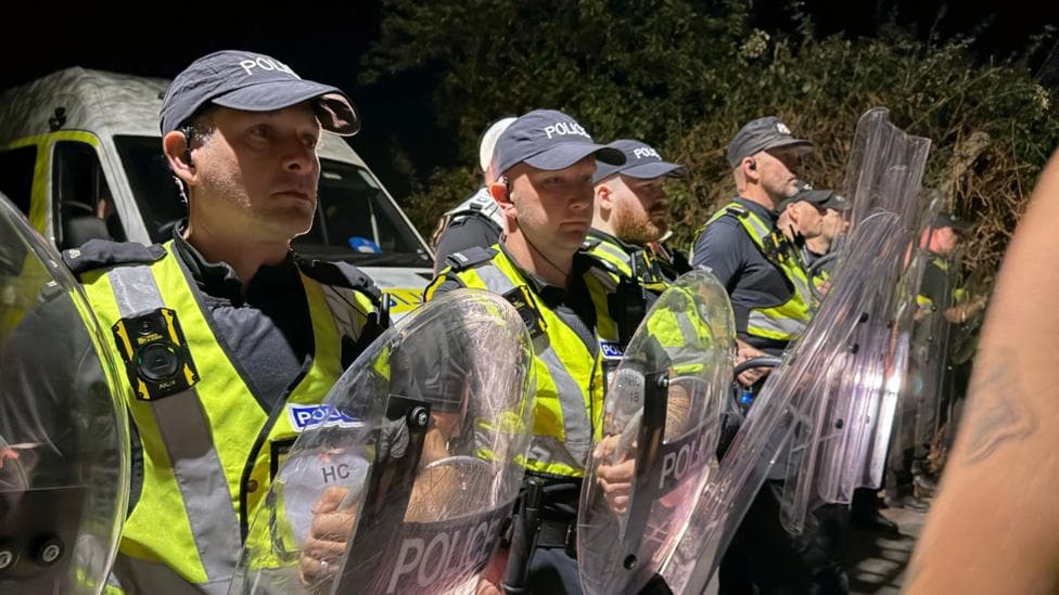 A row of police officers in high vis and holding shields stood facing crowds.
