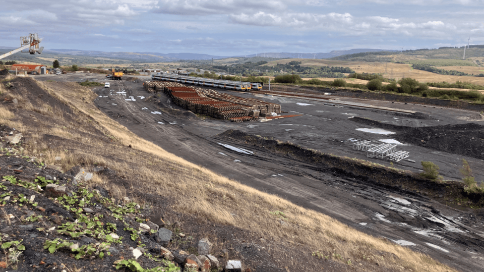 A large expanse of open space with two trains parked on half finished train tracks with diggers and other vehicles around the sides