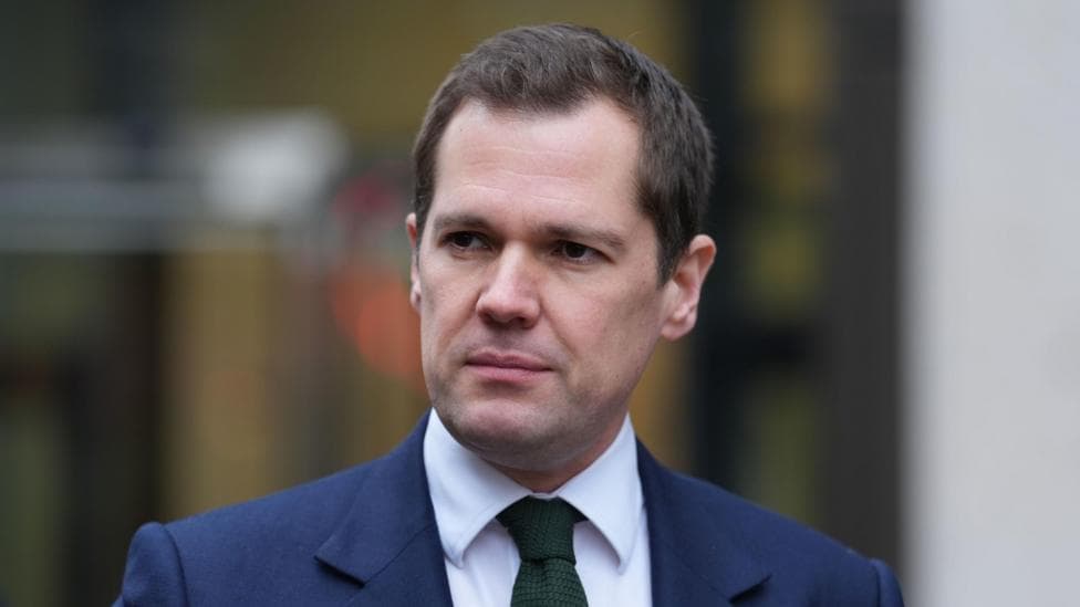 Robert Jenrick is wearing a blue suit jacket, white shirt and green tie.