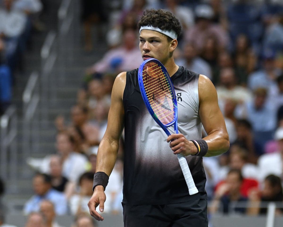 Ben Shelton holds his racket near his face, looking off to the side during a match