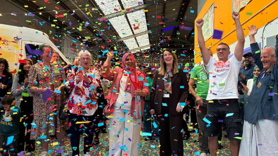 A group of people stand in a row and cheer as colourful confetti falls around them.