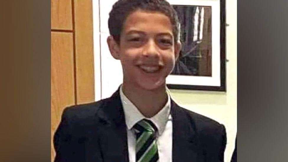 Noah Donohoe, a boy with dark hair, wearing a black blazer, with a white shirt and green, black and white tie.