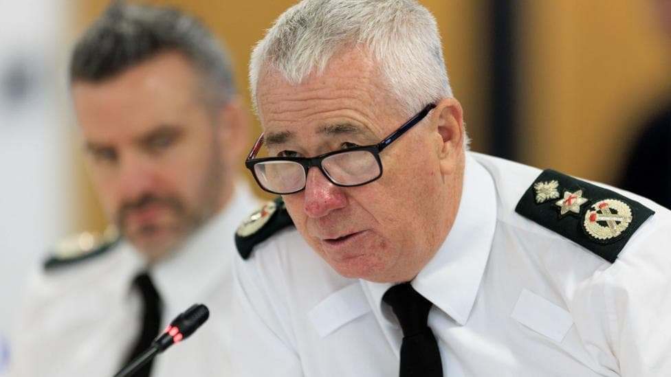 Man in PSNI uniform with grey hair, white shirt and is wearing a black tie.