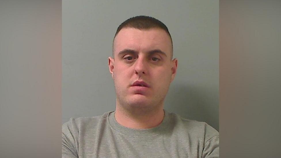 Mugshot of man with short dark hair and a grey sweater