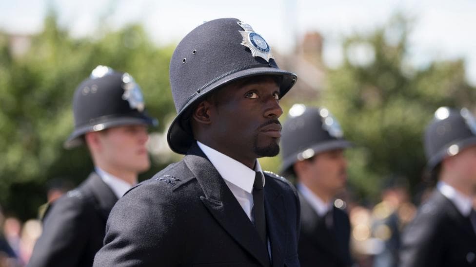 PC Idominik Efeotor in full police uniform in 2014 with many other police officers in uniform in a blurred background.