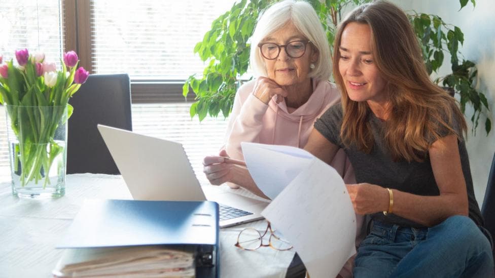 Two women look at bills and a laptop.