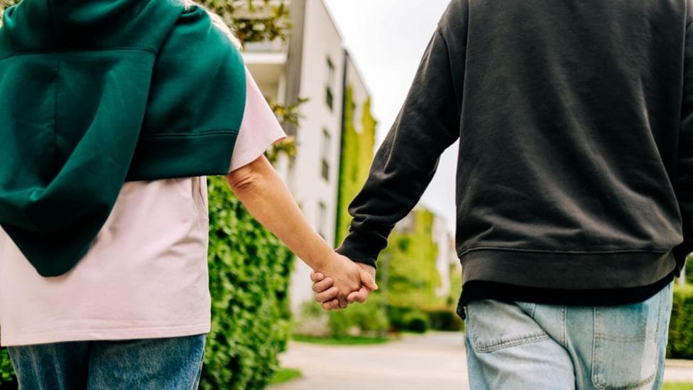 Two men, pictured from behind, holding hands.