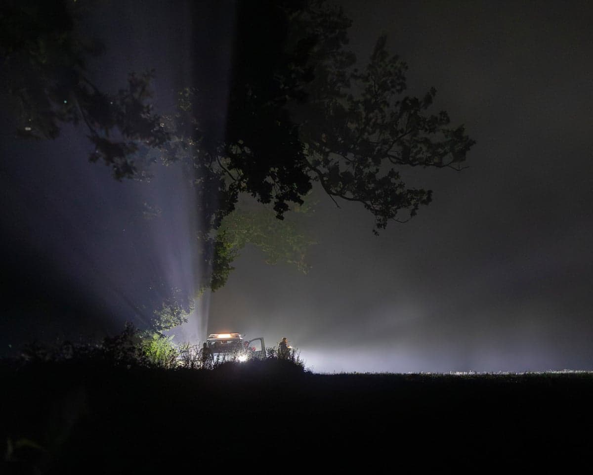 Lithuanian soldiers with vehicle lights secure a foggy field at night after a drone was shot down.