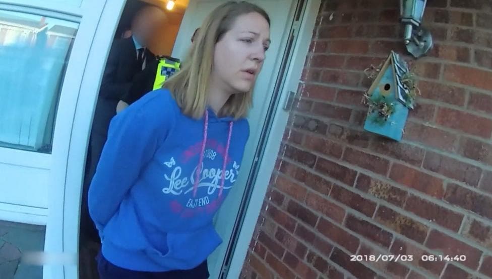 Image shows Lucy Letby, wearing a blue hooded top, being led in handcuffs from her house, in footage captured on a police body camera.
