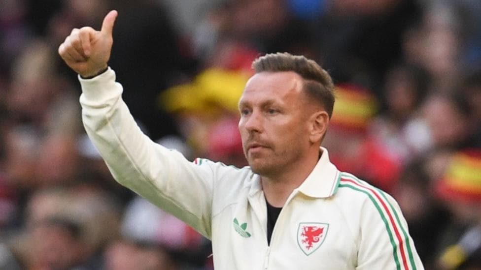Craig Bellamy on the touchline in a cream Wales top holds a thumb up