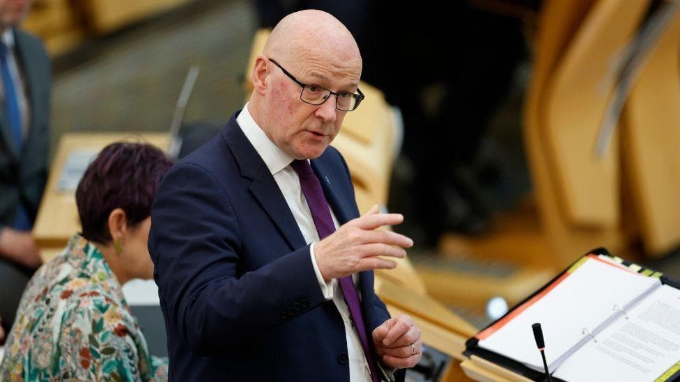 John Swinney, who is bald with glasses, speaking in the Scottish Parliament chamber.