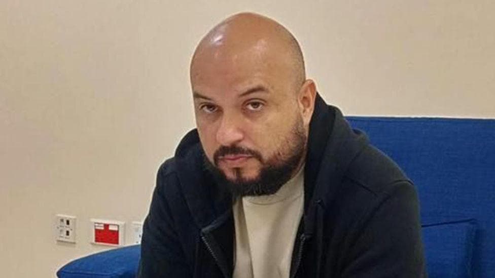 A head and shoulders image of Arturo Carrera Loaiza wearing a dark, warm jacket and white top. He is sitting on a blue chair.