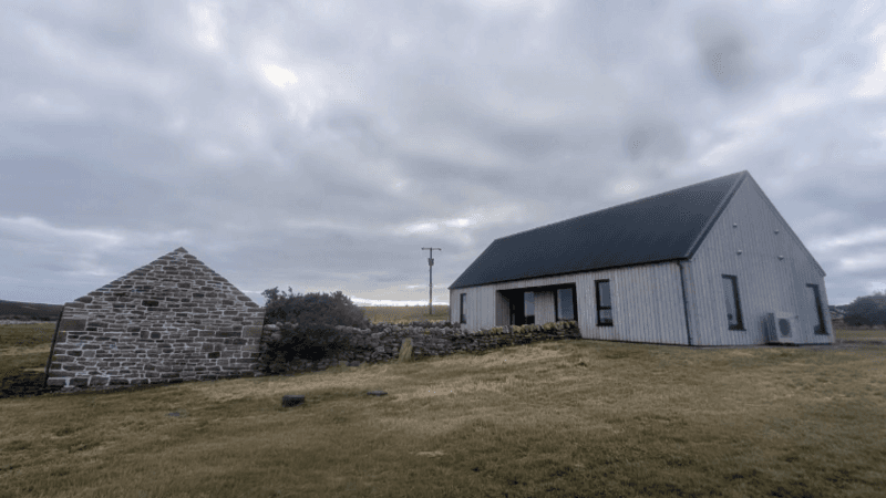 a single storey cottage next to a small outhouse in a field