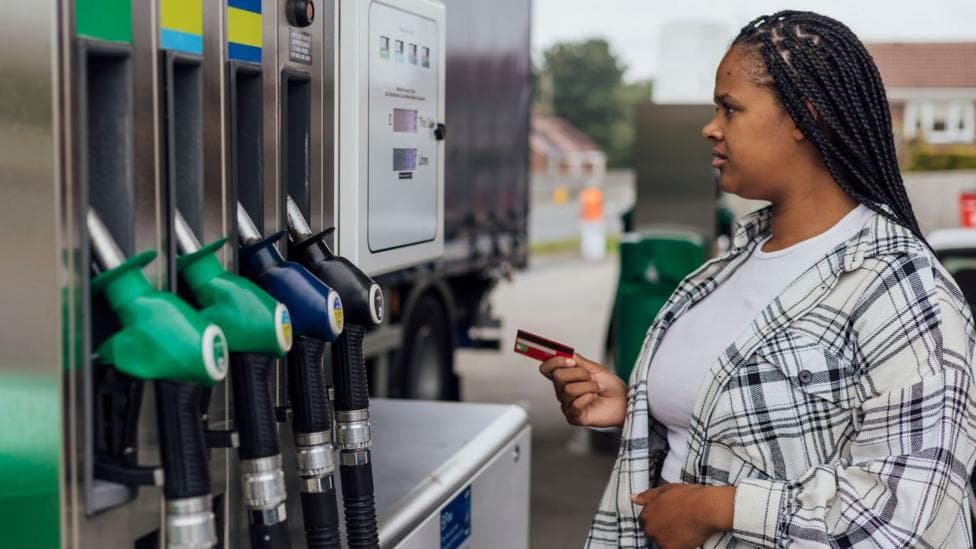 Young woman prepares to pay for fuel at the pump in a petrol station. She is wearing a checked black and white shirt over a white t-shirt