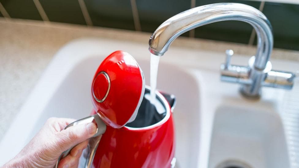 A person filling up a red kettle from the kitchen sink