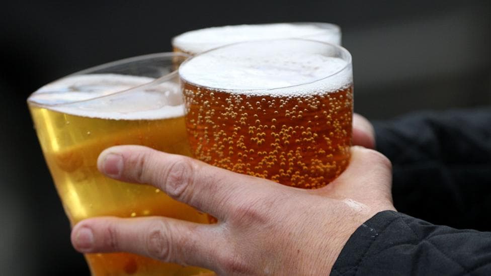 This is a close up image of a pair of hands holding three pints of what looks like beer or cider.