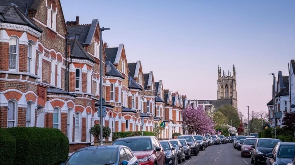 A street in Wandsworth with terraced houses on either side and cars parked on both sides of the road. There is a church in the background.
