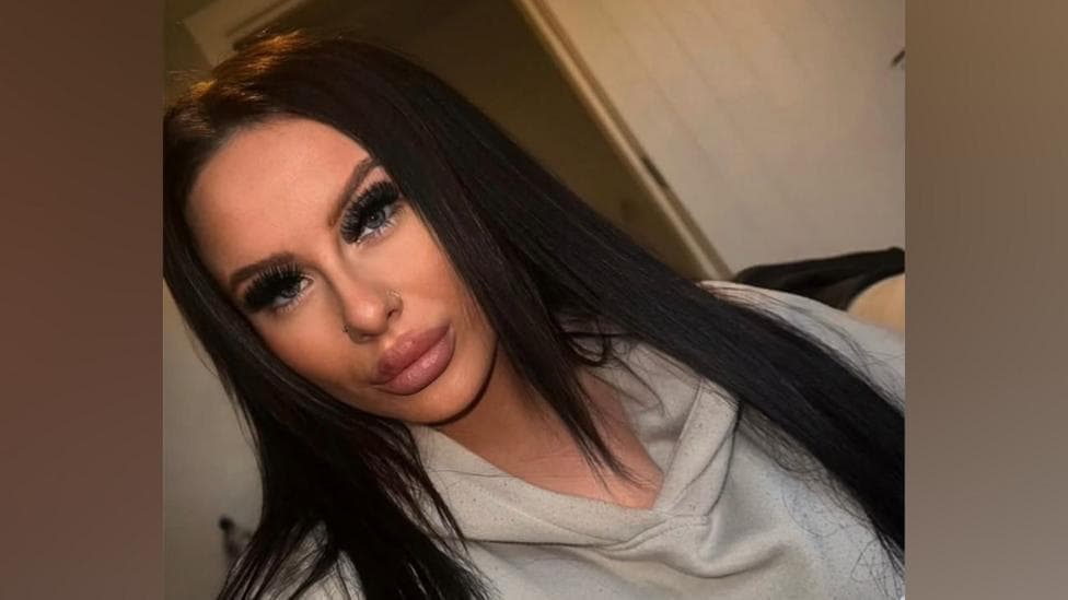 The image is a selfie of Emma Ashfield. She has long straight dark hair and is dressed in a grey hoody.