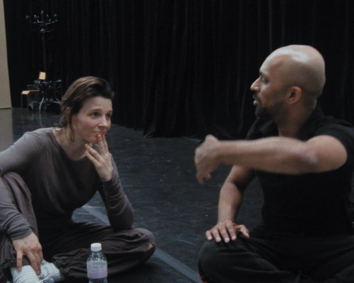 Juliette Binoche and Akram Khan sit cross-legged on a floor, facing each other in conversation