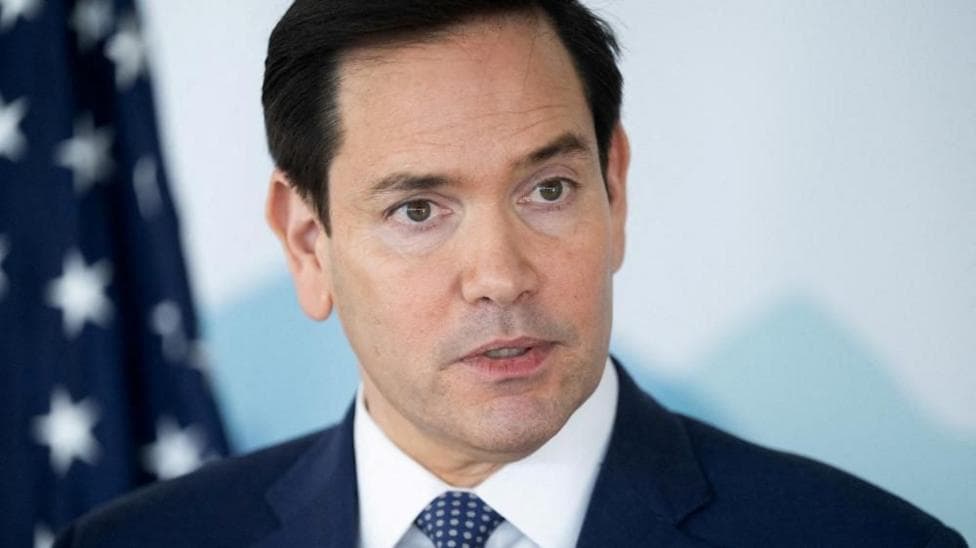 A close-up of Marco Rubio wearing a dark suit with white shirt and dotted tie