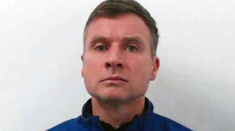 Head-and-shoulders portrait of a person wearing a blue zip-up jacket against a plain light-colored background, facing the camera with a neutral expression.
