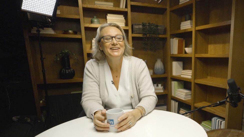 Nicole Leverich sitting at a table in a podcast studio with a mug on the table