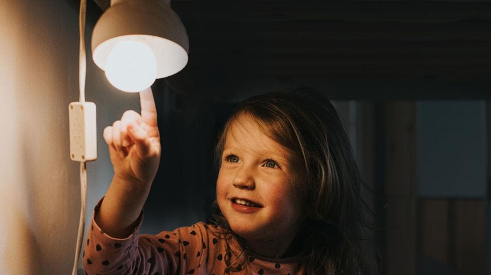 A young girl with long brown hair wearing a peach coloured top with black polka dots. She is pointing to a light.