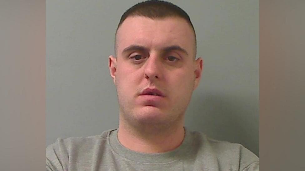 Mugshot of man with short dark hair and a grey sweater