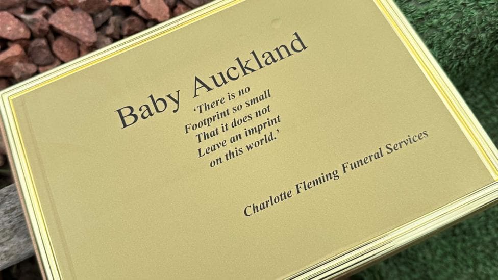 Close up of a gold plaque that reads: Baby Auckland. There is no footprint so small that it does not leave an imprint on this world. Charlotte Fleming Funeral Services.