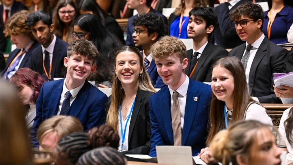 Members of Youth Parliament smile while sat on the benches of the House of Commons.
