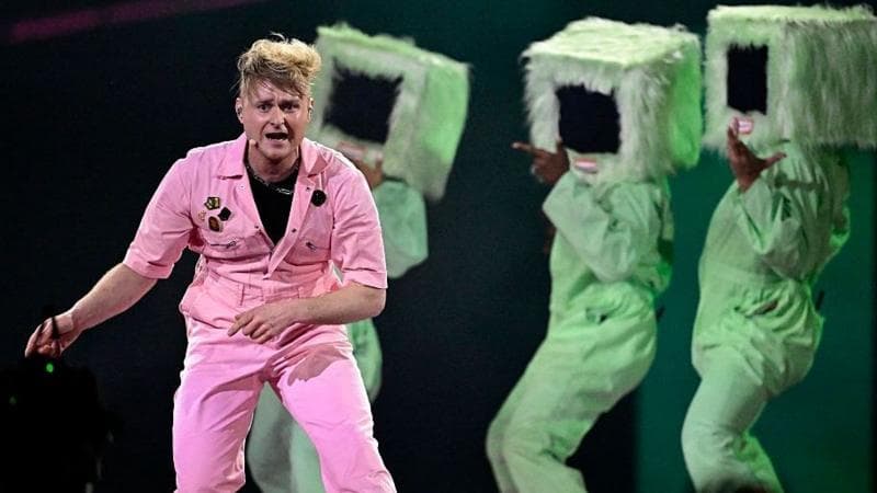 English musician Sam Battle, aka Look Mum No Computer, representing Great Britain with the song 'Eins, Zwei, Drei', performs during the second semi-final of the Eurovision Song Contest 2026. He's wearing a pink jumpsuit while three backing singers behind him wear furry monitor-shaped headgear.
