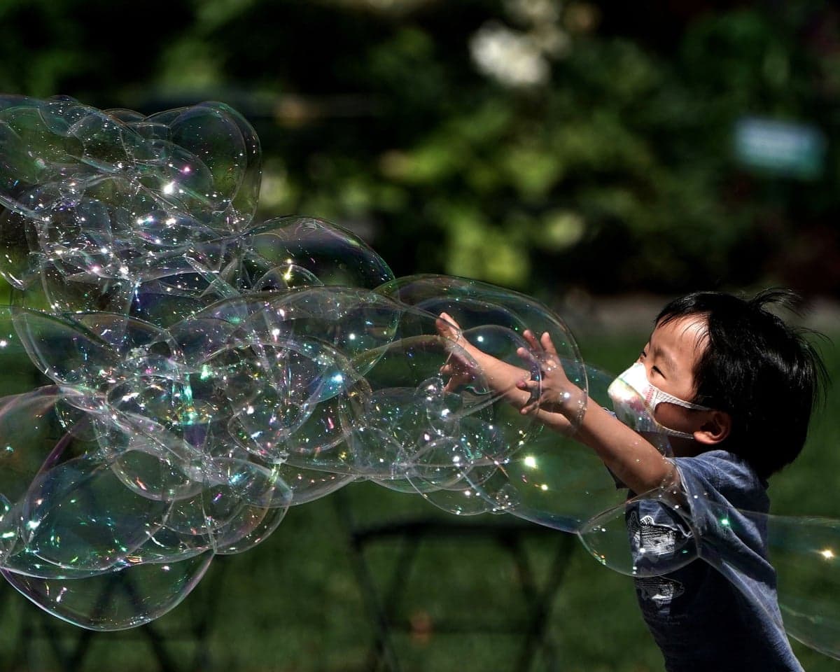 A child playing a park reaches out towards large soap bubbles in the air