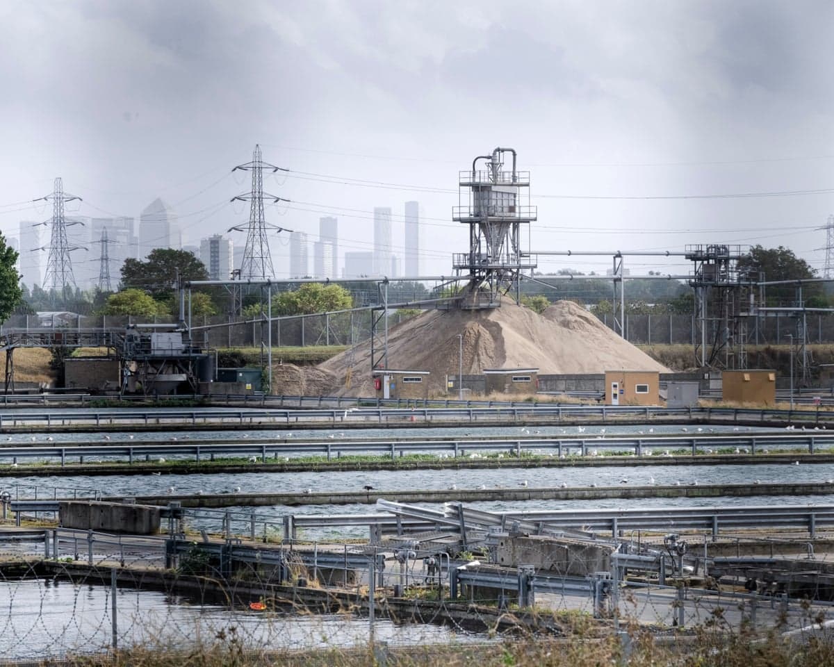 Thames Water’s Coppermills water treatment works, east London: a view across pools of water and industrial buildings on a grey day with the outlines of skyscrapers in the background.