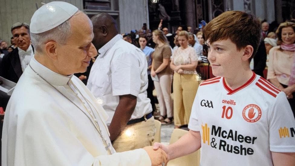 Pope Leo on the left shaking hands with Eoghan, a boy Auburn hair, wearing a Tyrone gaelic football jersey.