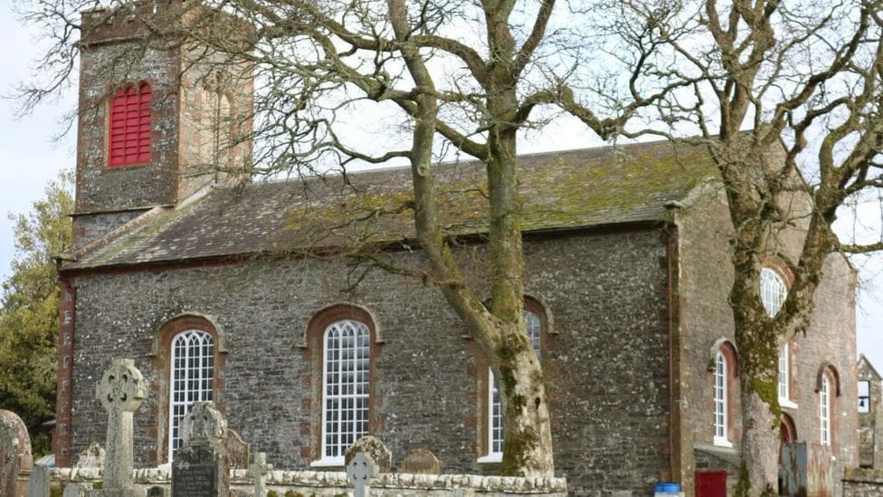 An old church building behind trees in a graveyard