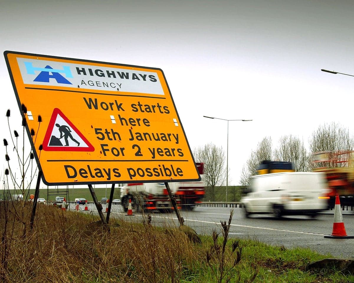 Cars drive past a sign on the M25 motorway informing them of road works