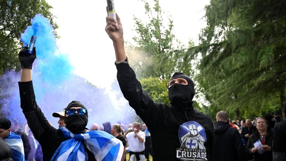 two men in black balaclavas and black clothes holding up flares