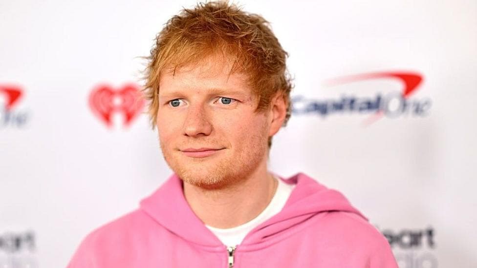 Singer Ed Sheeran poses for red-carpet arrivals in New York in 2025 wearing a pink hoodie and white shirt.