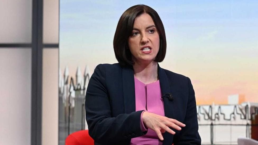 Bridget wears a navy blazer over a purple top sitting and talking in front of the illustrated Sunday with Laura Kuenssberg set.