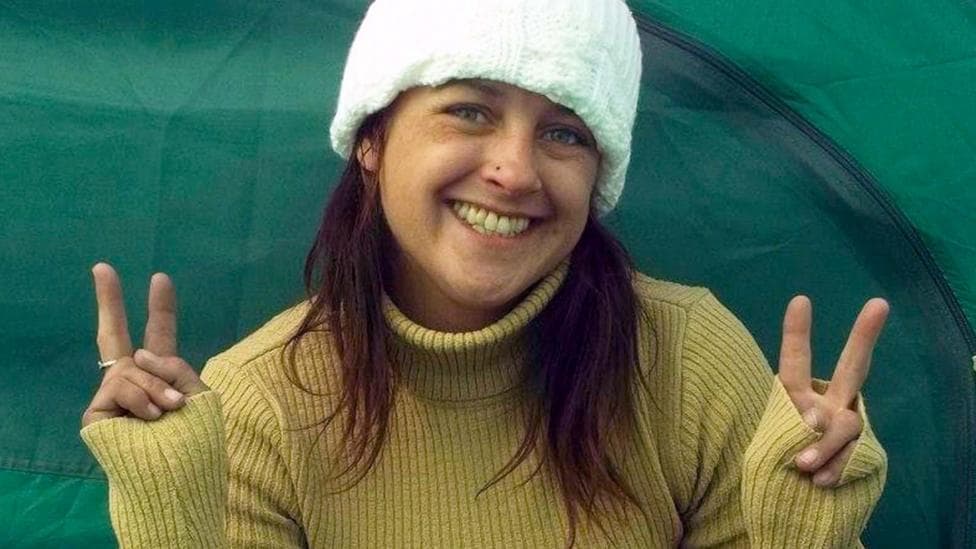 A woman smiles into the camera making peace signs with both hands