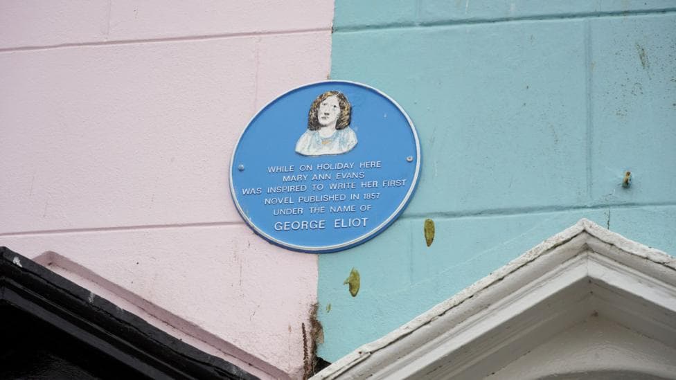 A blue plaque is seen on a blue and pink building